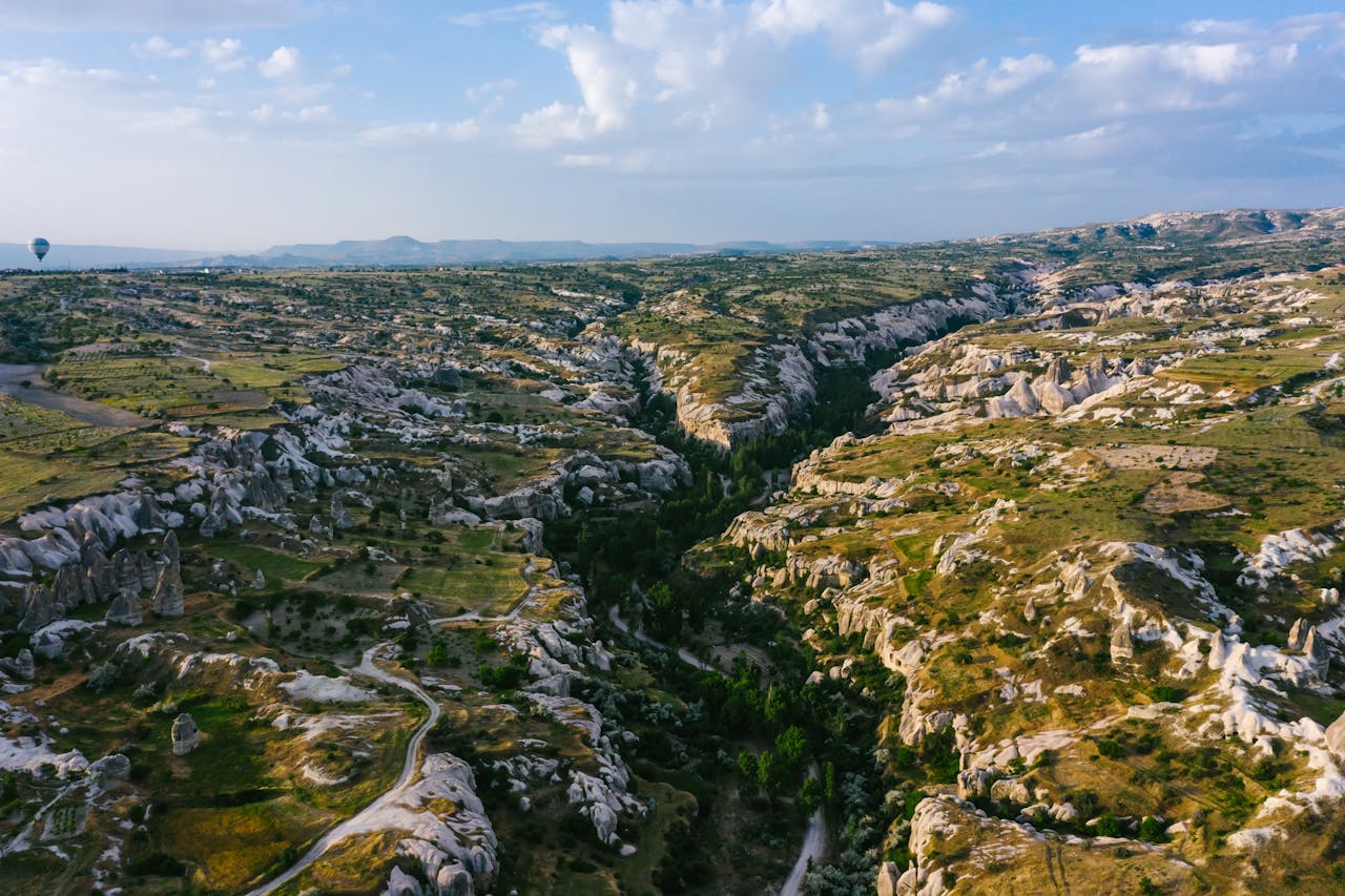 Stunning aerial shot of Cappadocia's rock formations and landscape with hot air balloon.